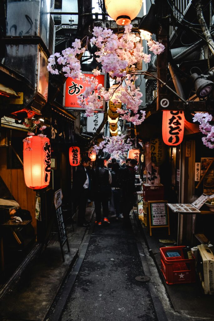 Explore a lively Japanese alley adorned with lanterns and cherry blossoms in an atmospheric street market.